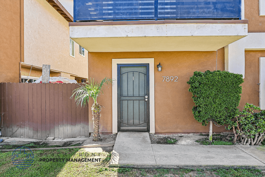 A brown house with a grey door and a palm tree in front.